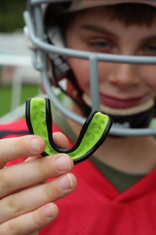 boy-in-a-football-helmet-smiling-holding-a-green-mouthguard